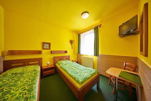 a yellow room with two beds and a table and a desk at Pension & restaurace Zelený Mlýn Žacléř in Žacléř