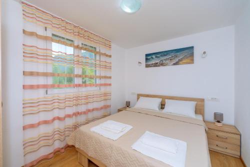 a white bedroom with a bed and a window at Apartments EcoNature in Virpazar