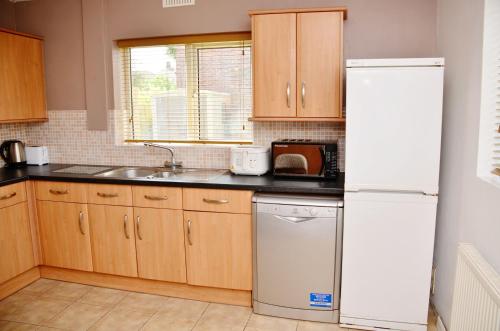 a kitchen with wooden cabinets and a white refrigerator at 1FG Dreams Unlimited Serviced Accommodation- Staines - Heathrow in Stanwell