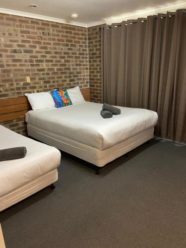 two beds in a room with a brick wall at Lake Albert Motel in Meningie