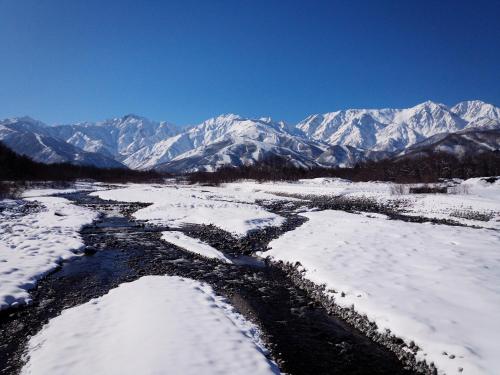 a snowy river with snow covered mountains in the background at Hakuba Highland Hotel in Hakuba