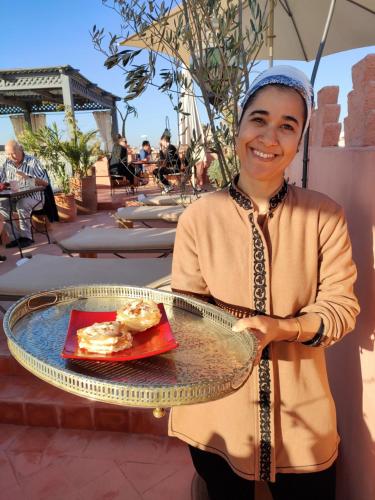 a woman holding a tray with a plate of food at Dar Andamaure in Marrakech