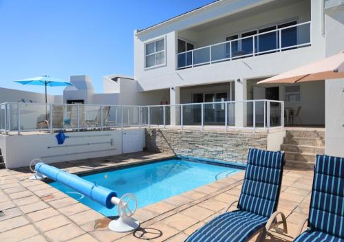 una piscina con 2 sillas y una casa en Zeezicht Apartments, en Stompneusbaai