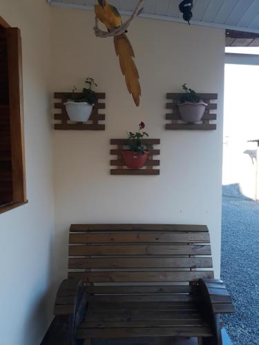 um banco de madeira contra uma parede branca com vasos de plantas em Pousada e Restaurante Redivo em Lauro Müller