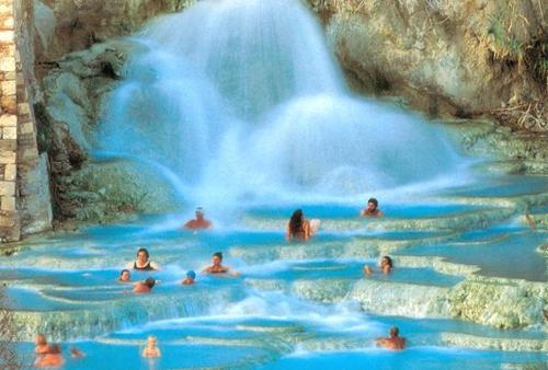 a group of people swimming in the water in front of a waterfall at B&B Il Giardino Etrusco in Saturnia