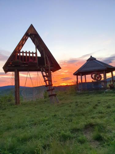 a gazebo and a building in a field with the sunset at Log cabin Uvac (Vikendica Saponjic) in Nova Varoš