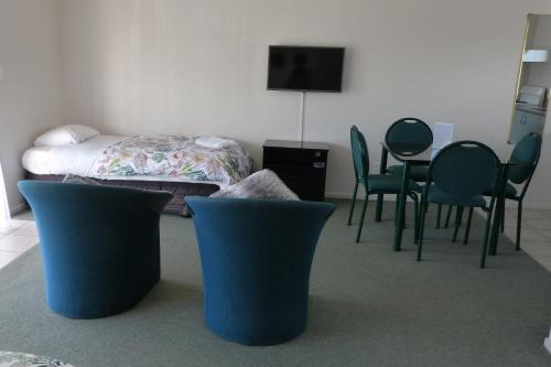a room with chairs and a bed and a table at Blake Court Motel in Whangamata