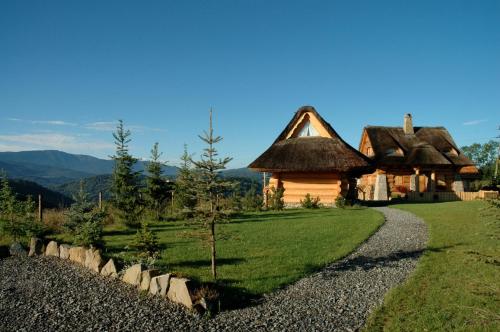 Cabaña de madera con techo de paja y camino de grava en Osada Beskidzka en Zawoja