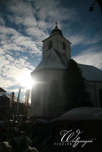 a church with a clock tower with the sun behind it at Pension Wolfgangsee in St. Wolfgang