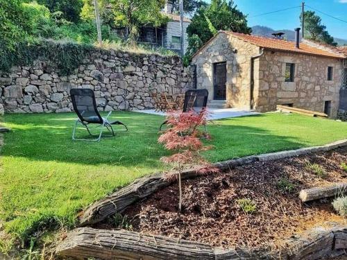 a yard with two chairs and a stone wall at River House Sejães in Oliveira de Frades