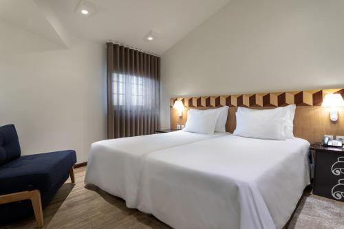a bedroom with a large white bed and a chair at Hotel Aveiro Center in Aveiro