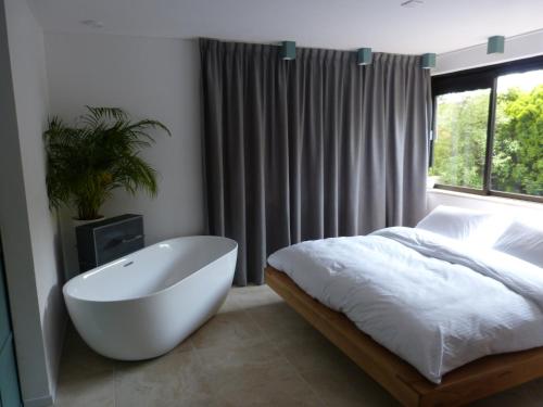 een slaapkamer met een wit bad, een bed en een raam bij Huize Triangel - Wellness studio met sauna in Noordwolde