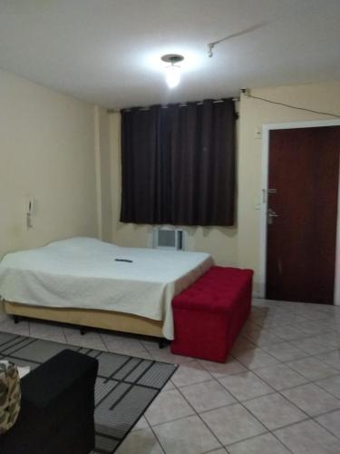a bedroom with a bed and a red ottoman and a window at Apto no Centro in Campos dos Goytacazes