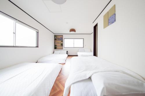 two beds in a room with white walls and windows at NexStay HOUSE Osaka West in Osaka