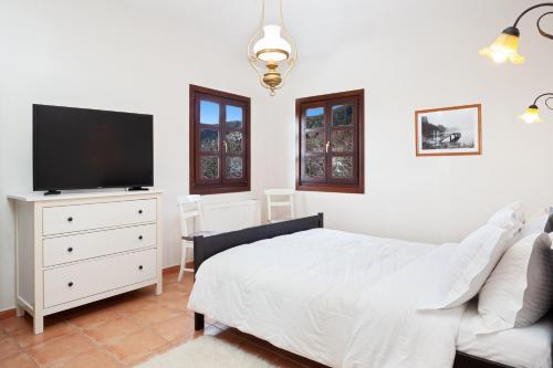 a white bedroom with a bed and a tv at Erofili Hotel & Suites in Portaria