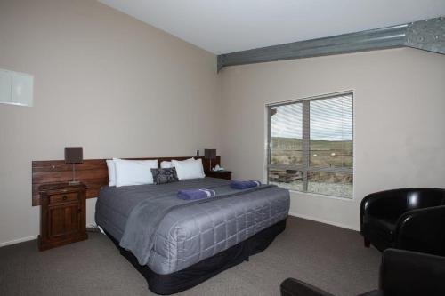a bedroom with a bed and a chair and a window at Tussock Lodge - Waipiata in Waipiata