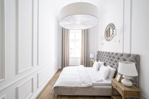 - une chambre blanche avec un lit et un grand lustre dans l'établissement Apartament Golden Place, à Cracovie