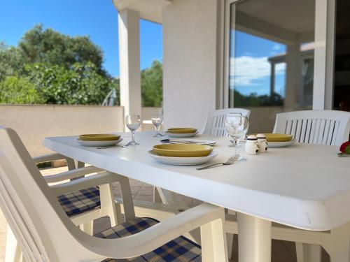 a white table with plates and wine glasses on it at Apartments Pijaza in Rab