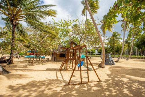 a playground with a swing set on a beach with palm trees at Xeliter Balcones del Atlantico - Las Terrenas in Las Terrenas