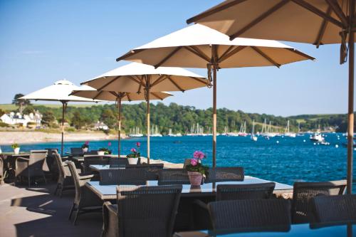 a group of tables and chairs with umbrellas next to the water at The Idle Rocks in Saint Mawes