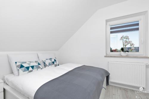 a white bedroom with a bed and a window at Jantar Apartamenty - Casa Francesco in Grzybowo