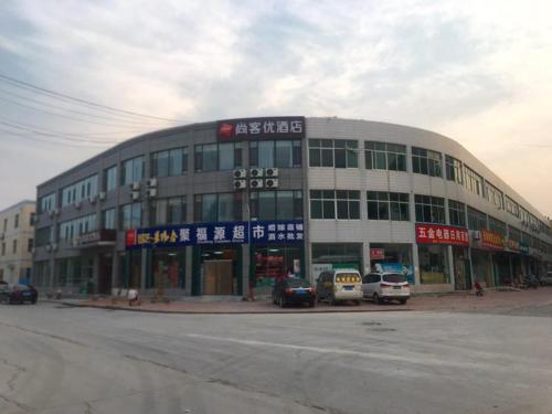 um grande edifício com carros estacionados em frente em Thank Inn Chain Hotel Weifang High-tech Zone Weifang East Expressway Intersection em Weifang