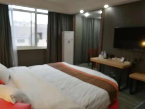 a hotel room with a bed and a desk and a television at JUN Hotels Zhejiang Jiaxing Haiyan Qiyuan North Road in Jiaxing