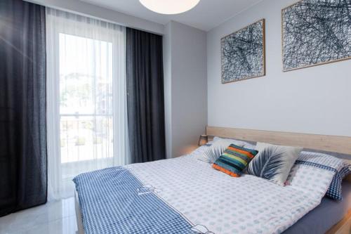 een slaapkamer met een bed met een blauwe deken en een raam bij Resort Apartamenty Klifowa Rewal 31 in Rewal