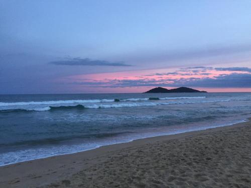 einen Strand bei Sonnenuntergang mit Wellen und einem Berg in der Unterkunft Paradise Container Glamping in Florianópolis