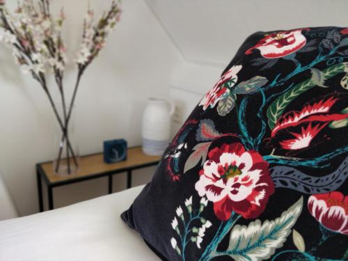 a black pillow with flowers on a bed with a table at Appartementen Dorp & Duin in Egmond aan Zee