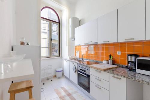 a kitchen with white cabinets and an orange tile wall at Cozy apartment at the city center in Figueira da Foz