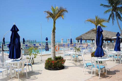 a group of tables and chairs with blue umbrellas and palm trees at Glunz Ocean Beach Hotel and Resort in Marathon