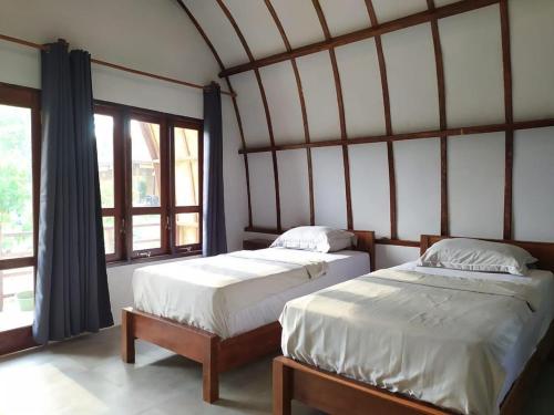 two beds in a room with a large window at Gino's Place - Bungalows and Restaurant in Bukit Lawang