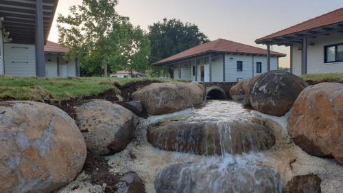 a waterfall in a yard with rocks and a house at כפר הנופש מעיין in Ma‘yan Barukh