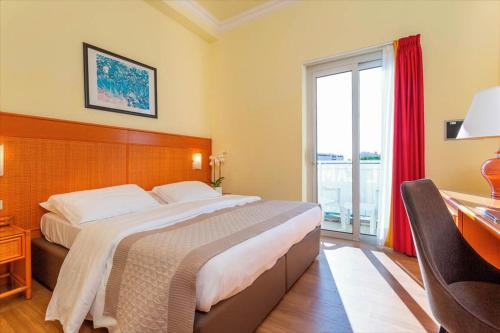 a bedroom with a bed and a desk and a window at Hotel Principe Palace in Lido di Jesolo