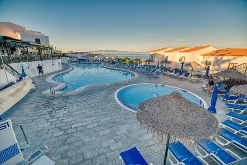 une grande piscine avec des chaises et des parasols bleus dans l'établissement Ona Las Rosas, à Puerto de Santiago