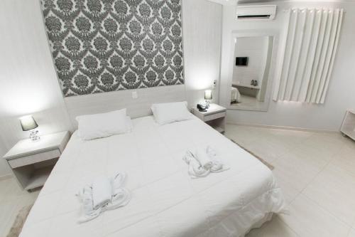 a white bedroom with a large white bed and a mirror at Olinda Hotel e Eventos in Toledo