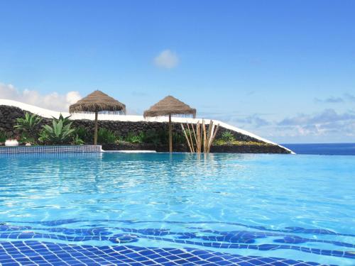 a swimming pool with umbrellas and the ocean at Wellshouses in Capelas
