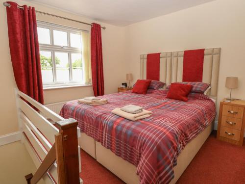 a bedroom with a bed with red curtains and a window at 2 Lock Cottages in Honing