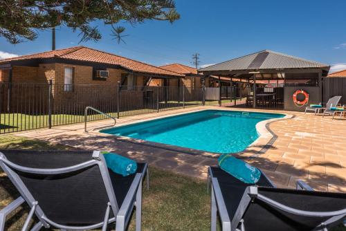 a swimming pool with two chairs in front of a house at Geraldton's Ocean West Holiday Units & Short Stay Accommodation in Geraldton