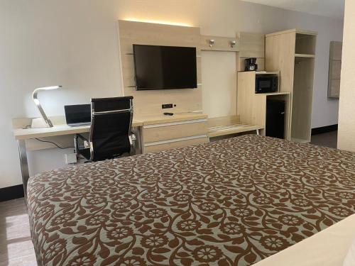 a hotel room with a bed and a desk and a tv at Days Inn & Suites by Wyndham Peachtree Corners Norcross in Norcross