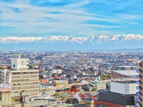 a city with snow covered mountains in the background at Takaoka Manten Hotel Ekimae in Takaoka