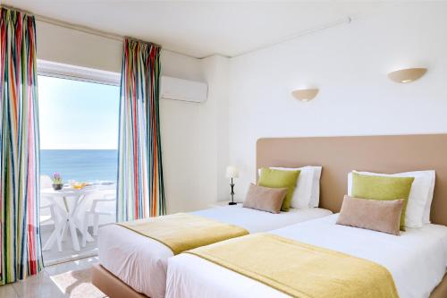 two beds in a room with a view of the ocean at Monica Isabel Beach Club in Albufeira