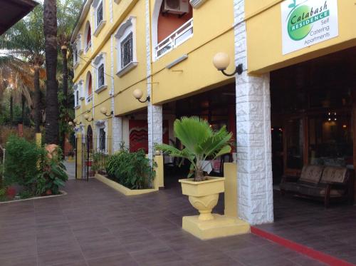 a yellow building with a plant in a pot on a sidewalk at Calabash Apartment-Hotel in Kotu
