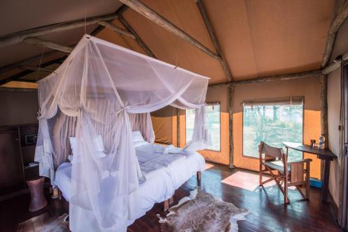 ein Schlafzimmer mit einem Himmelbett in einem Zimmer mit einem Tisch in der Unterkunft Chobe River Camp in Ngoma