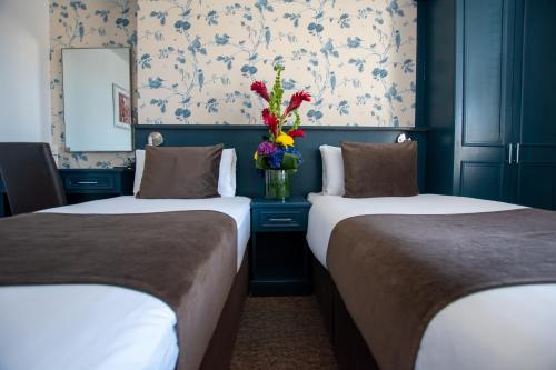 two beds in a room with a vase of flowers at New Steine Hotel - B&B in Brighton & Hove