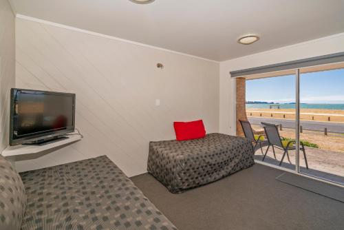 uma sala de estar com uma televisão, um sofá e uma cadeira em The Oceanside Motel em Whitianga
