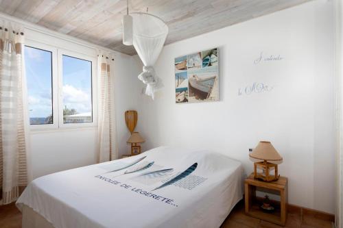 a white bedroom with a bed and a window at COEUR SUR LA MAIN in Le Diamant