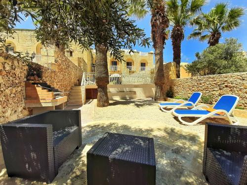 a patio with chairs and a tv and palm trees at Blossom Farmhouses in Għasri