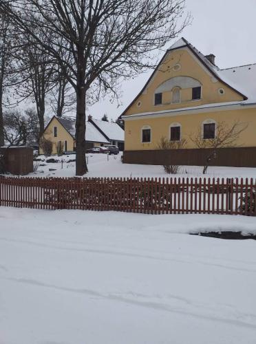 a yellow house with a fence in the snow at Apartmány Dolní Moravice in Dolní Moravice